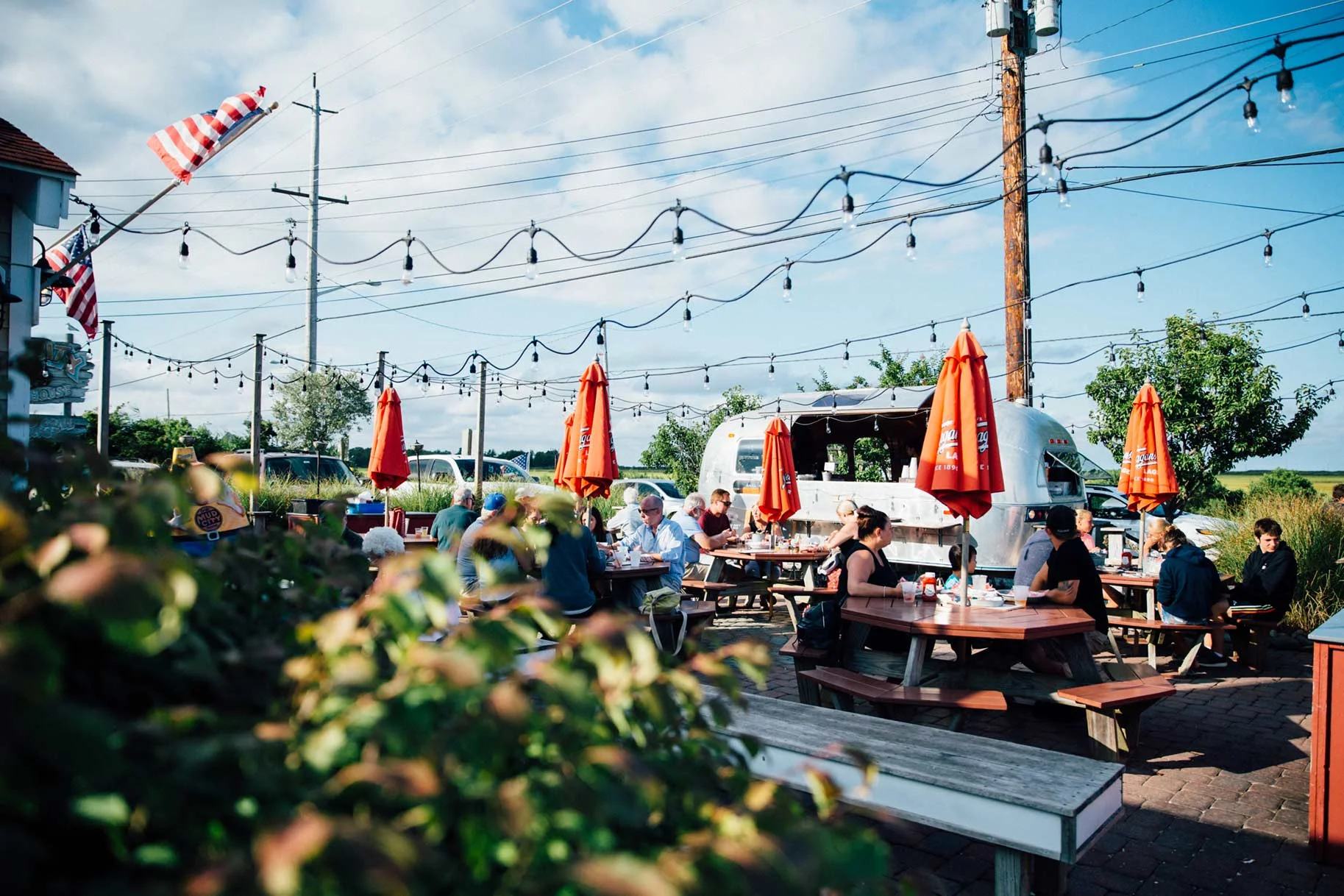 Outdoor patio dining at Mud City with Airstream bar and orange umbrellas
